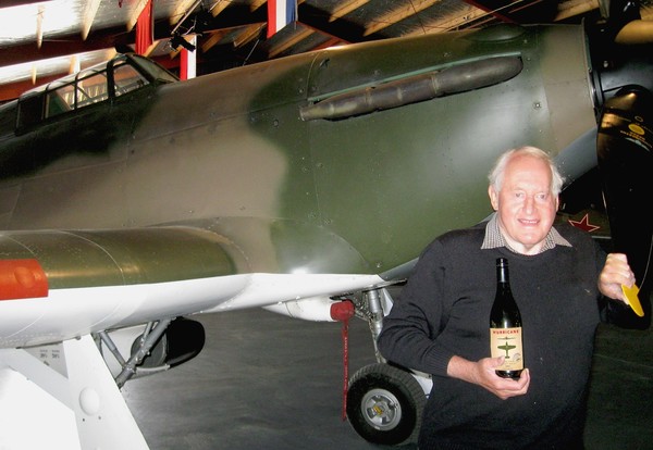 Sir Tim Wallis holding the first bottle of the Warbirds Over Wanaka Hurricane Pinot Gris while standing in front of his AFC Hawker Hurricane MkIIA.
